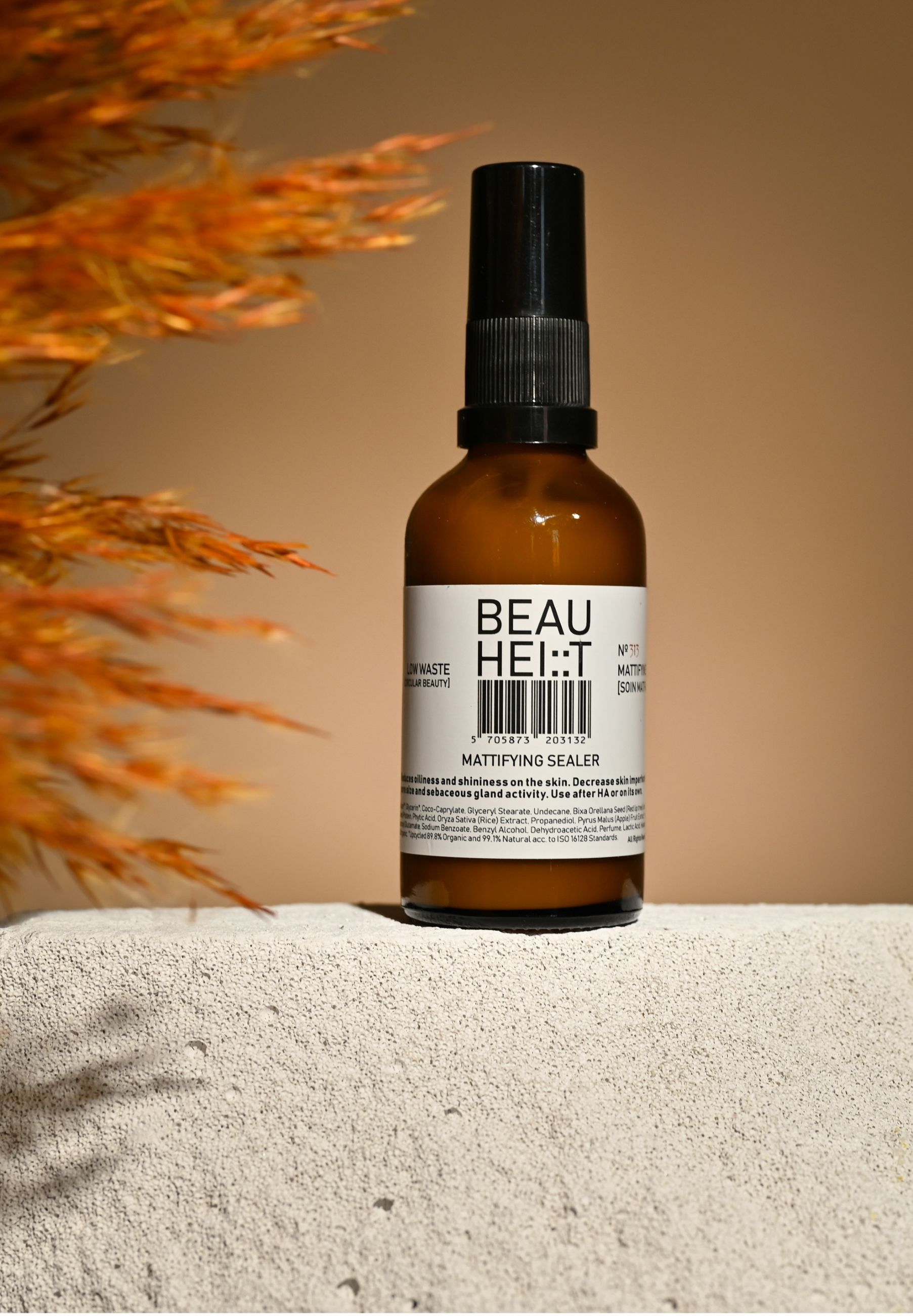Braune Glasflasche mit schwarzem Sprühkopf. Etikett mit Produktnamen und Barcode. Text: Mattifying Sealer. Hintergrund: Beige, mit Pflanzen.