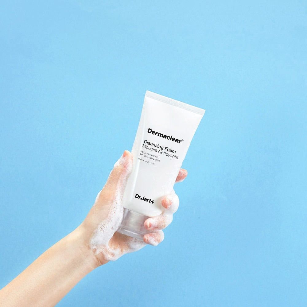 Weiße Tube mit Produktnamen und Schriftzug. Hand hält Tube mit Schaum. Hintergrund blau.