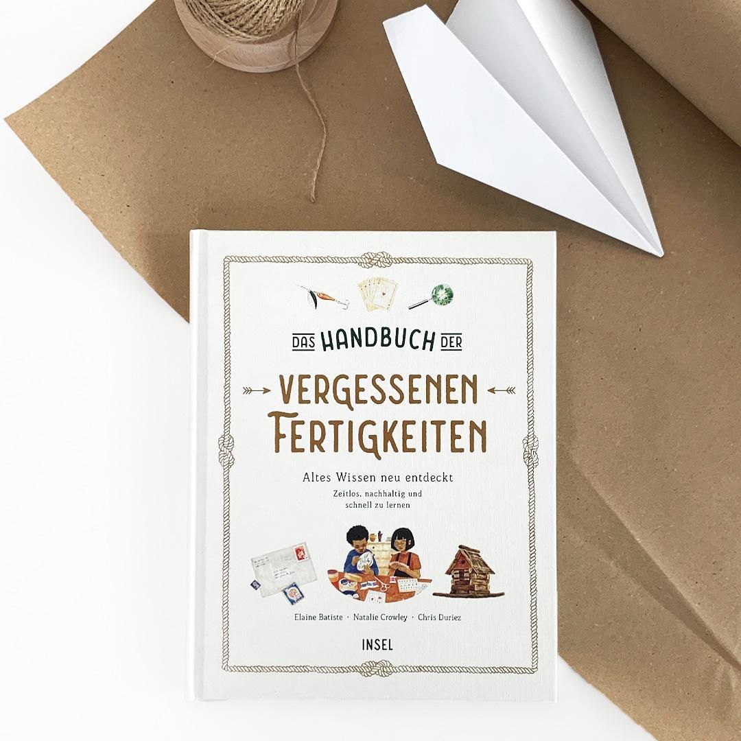 Buch mit weißem Einband. Titel: Das Handbuch der vergessenen Fertigkeiten. Illustrationen von Kindern, Briefen, Haus. Auf braunem Papier.