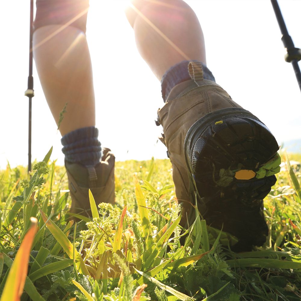 Persoon in wandelschoenen loopt over een grasveld. Zonlicht op de achtergrond. Schoenen met profielzool.