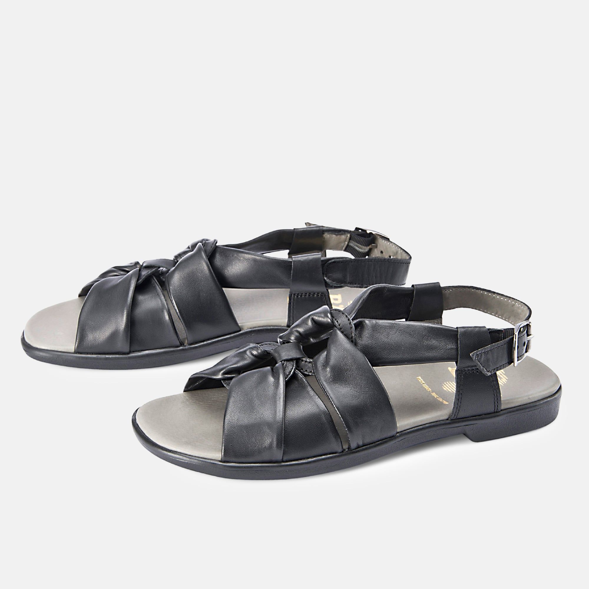 Schwarze Sandalen mit breitem Riemen, Schnalle und gekreuzten Riemen. Graue Innensohle. Zwei Sandalen nebeneinander.