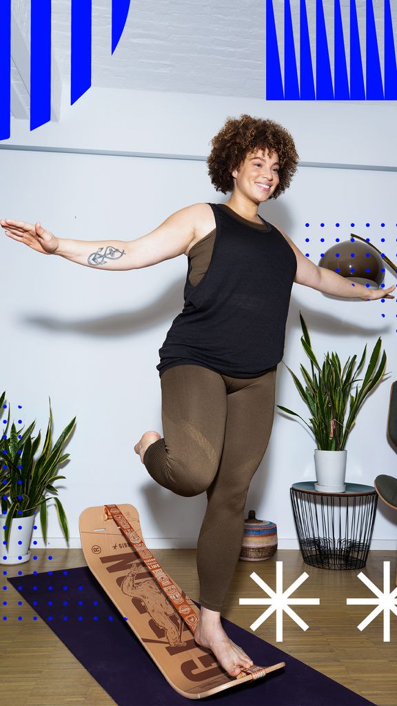 Frau balanciert auf einem Balance Board. Sie steht auf einem Bein, Arme seitlich ausgestreckt. Yoga-Matte.