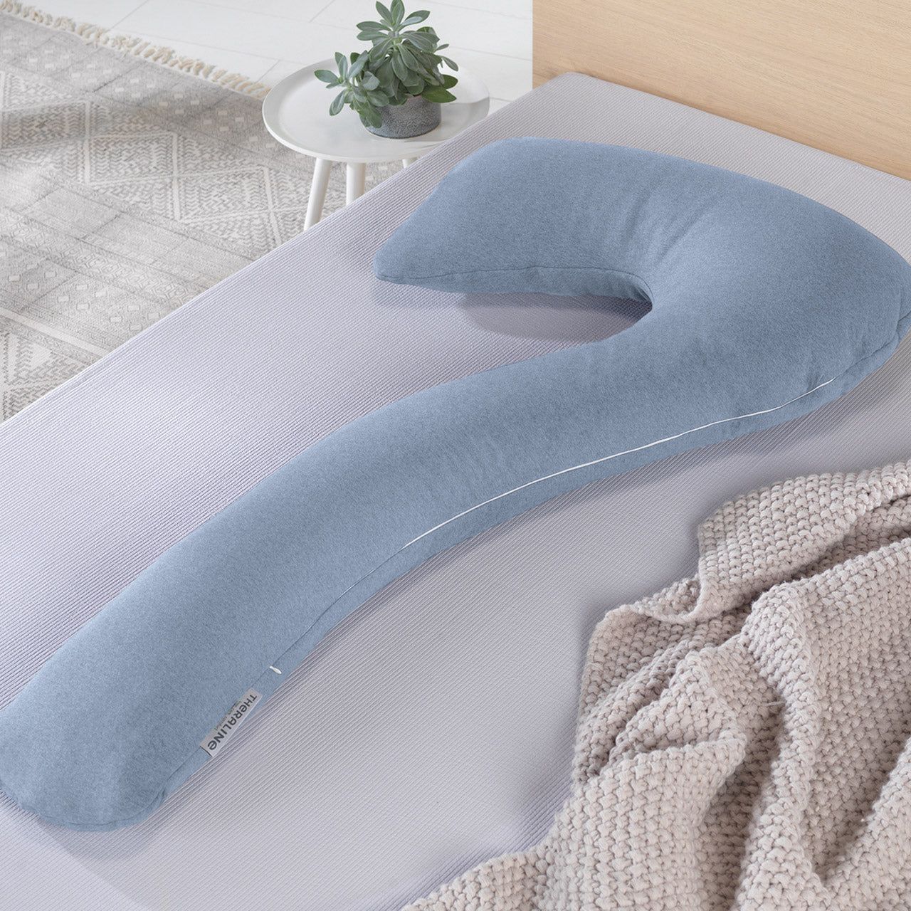 Blau-graues Seitenschläferkissen auf Bett. Weißer Streifen entlang der Kante. Theraline-Label.