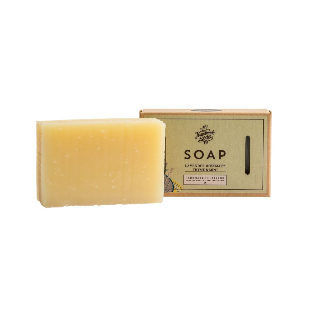 Hellgelbes Seifenstück neben Kartonverpackung. Aufschrift: Lavendel, Rosmarin, Thymian, Minze. "The Handmade Soap Company".