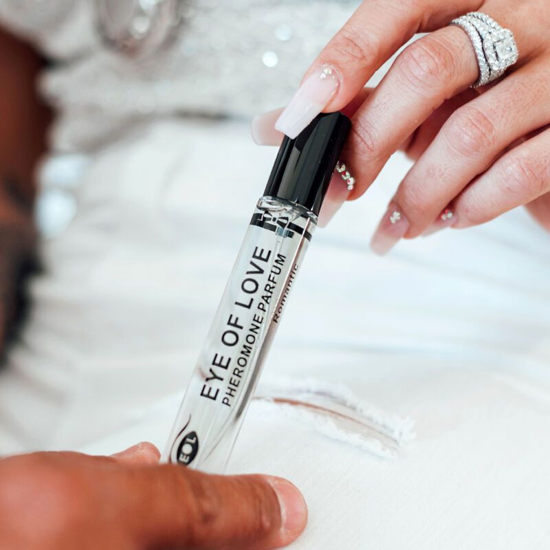 Eine Hand hält eine Parfümflasche. Aufschrift: EYE OF LOVE Pheromone Parfum Romantic. Eine andere Hand berührt die Person.