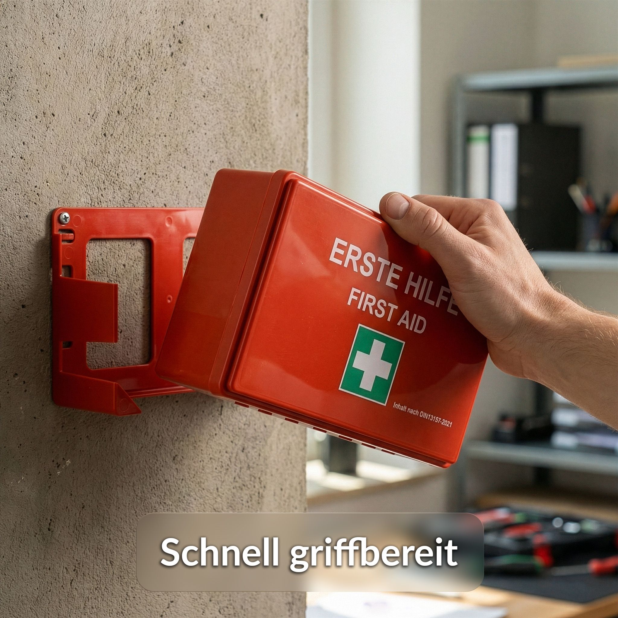 Roter Erste-Hilfe-Koffer an Wandhalterung. Aufschrift: Erste Hilfe/First Aid. Grünes Kreuz. Schnell griffbereit.