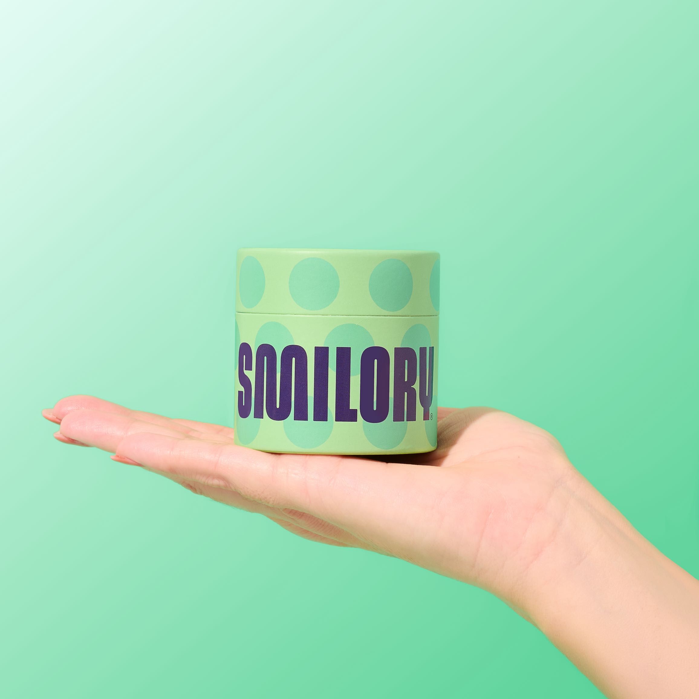 Grüner Zylinder mit „SMILORY“-Schriftzug in einer Hand. Grüner Hintergrund.