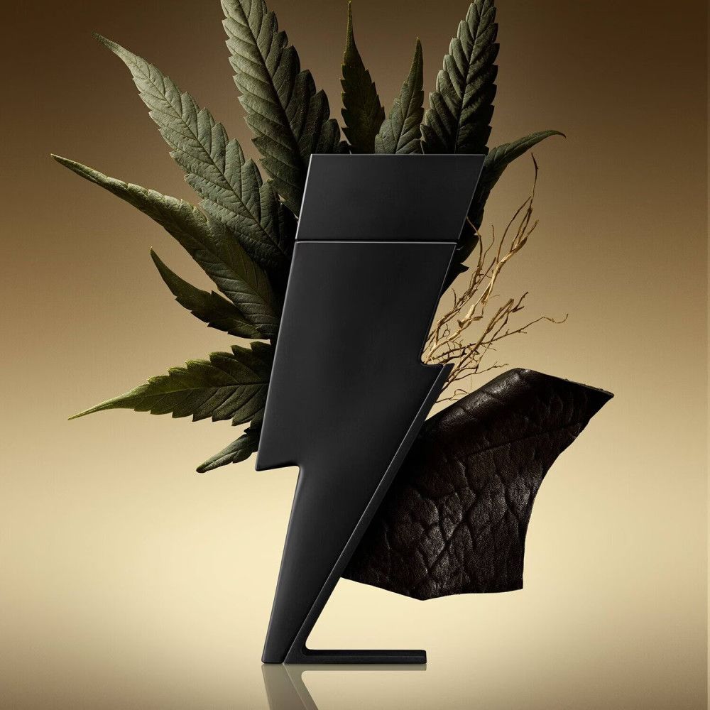 Schwarzer Flakon in Blitzform, umgeben von Blättern und Zweigen. Goldfarbener Hintergrund.