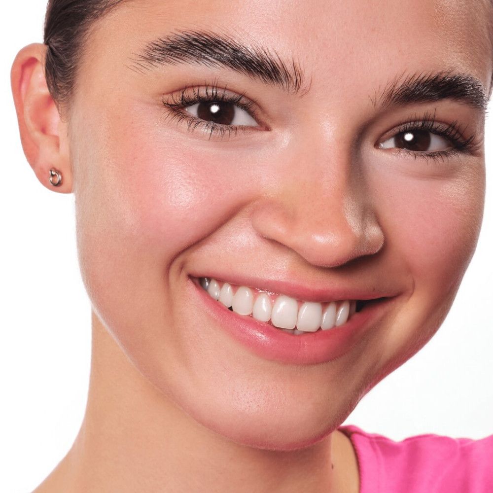 Porträt einer lächelnden Frau. Sie hat braune Augen und trägt rosa Oberteil. Haut ist ebenmäßig.