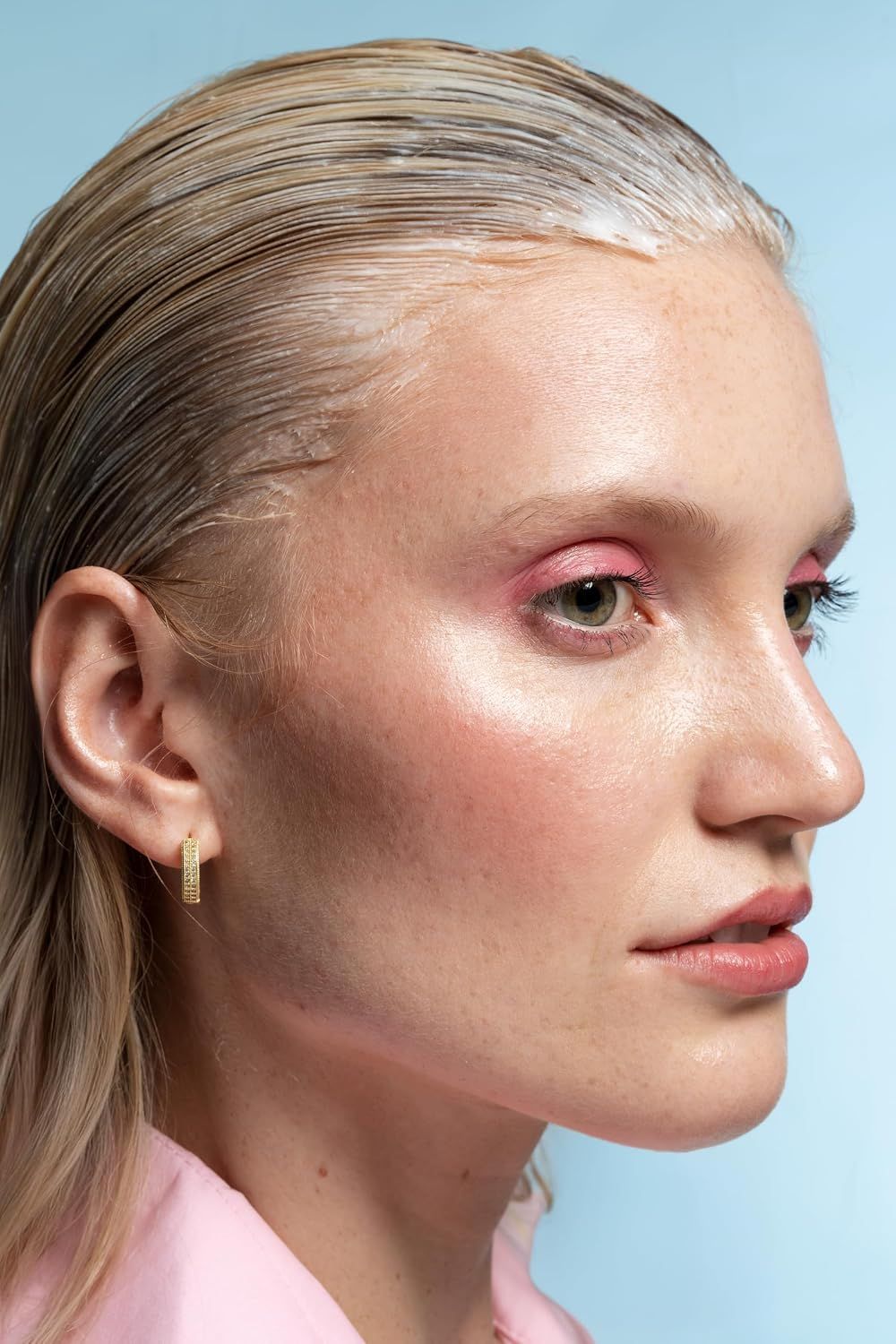 Frau mit blonden Haaren und Make-up, trägt ein pinkes Oberteil.