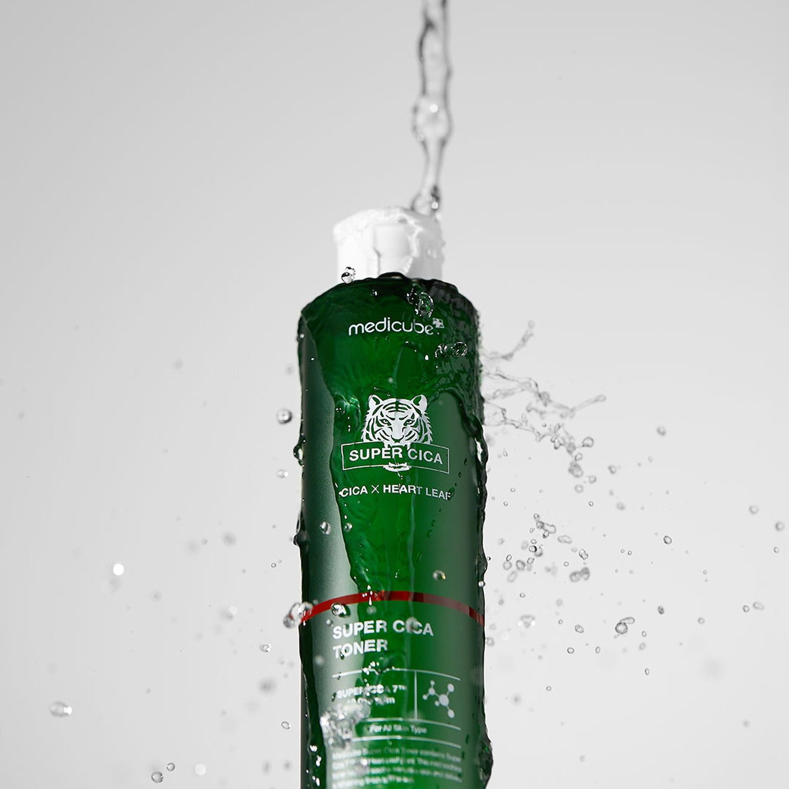 MEDICUBE Super Cica Toner Flasche, die von Wasserspritzern umgeben ist.