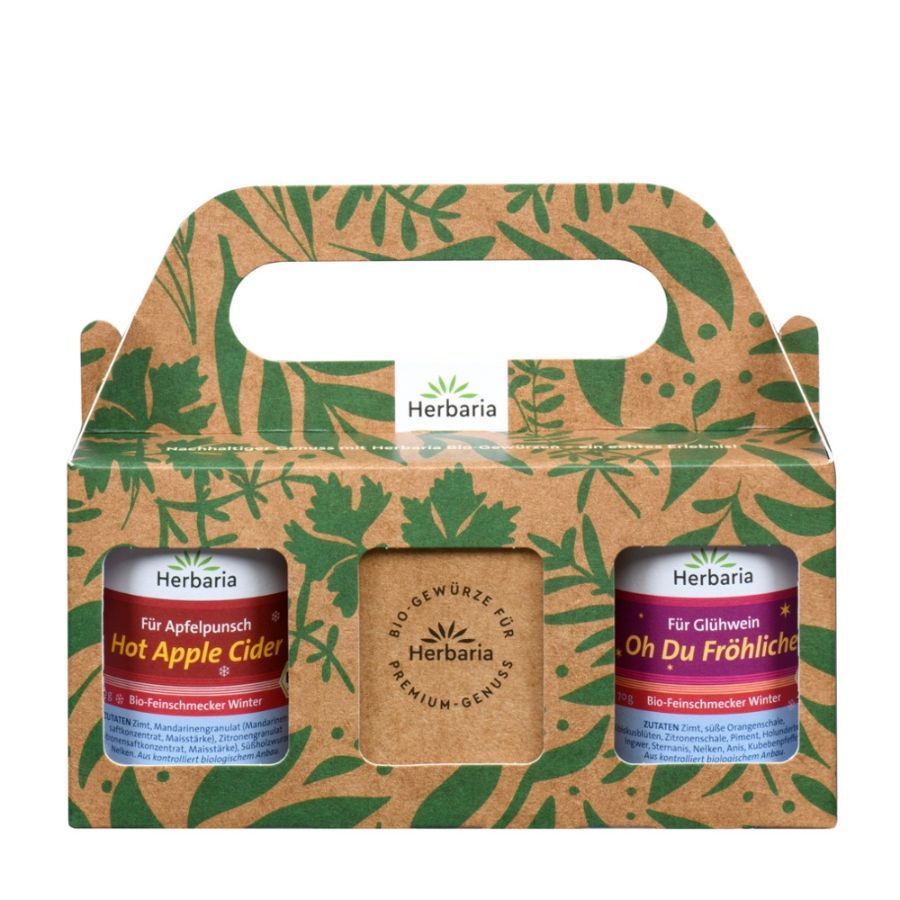 Geschenkset mit zwei Dosen und einem Block. Aufschrift: Herbaria, Hot Apple Cider, Oh Du Fröhliche. Verpackung mit Griff und Blättermuster.