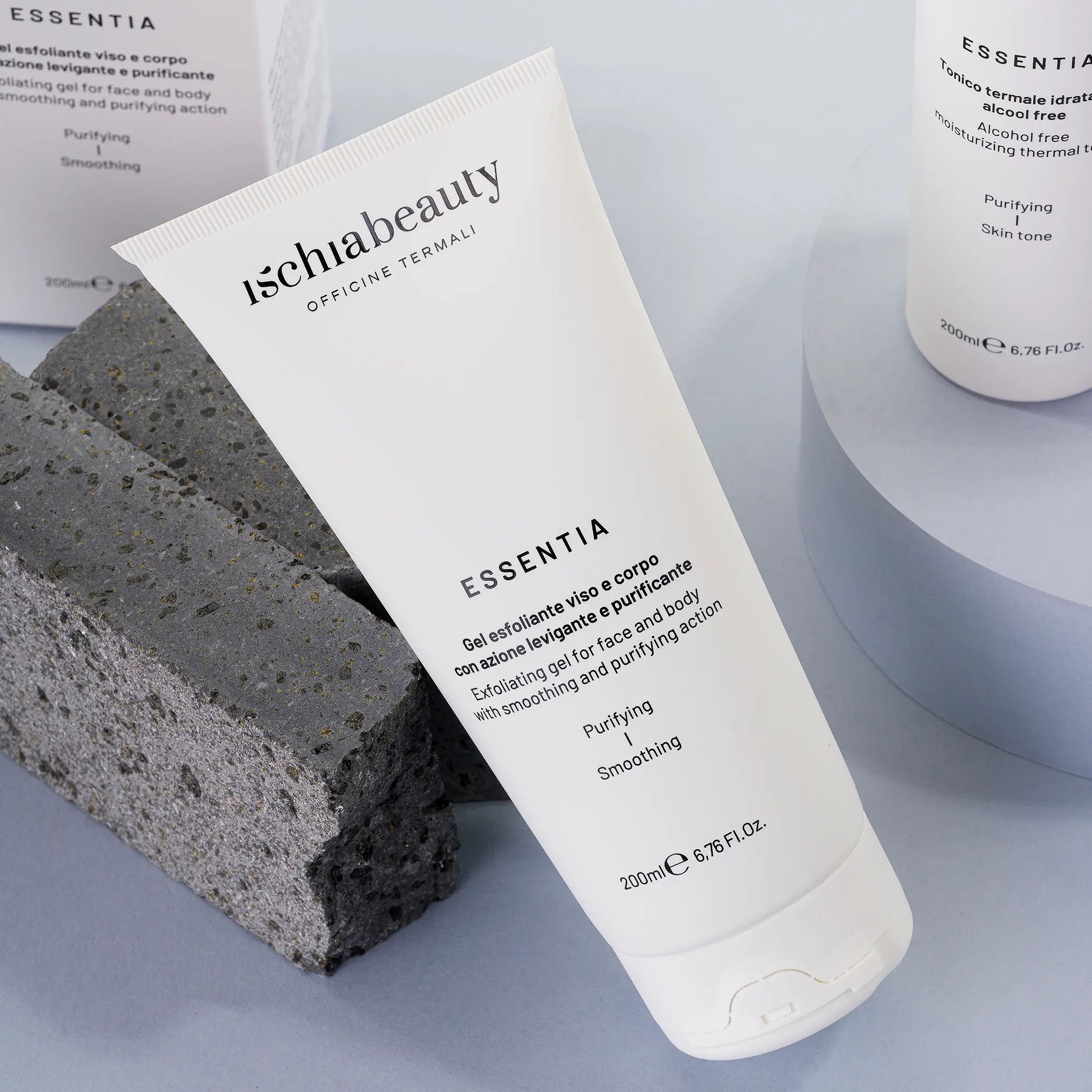 Weiße Tube mit Produktbeschriftung. Text: Ischiabeauty, Essentia, Gel esfoliante viso e corpo. Auf Steinblock platziert, neben einer weiteren Tube.