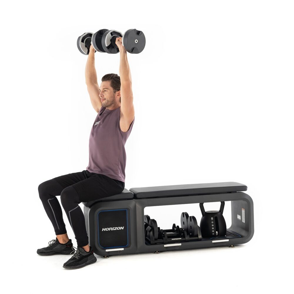 Mann trainiert mit Hanteln auf Fitnessbank. Graue Bank mit Horizon-Logo. Kettlebell und Hanteln in der Ablage.