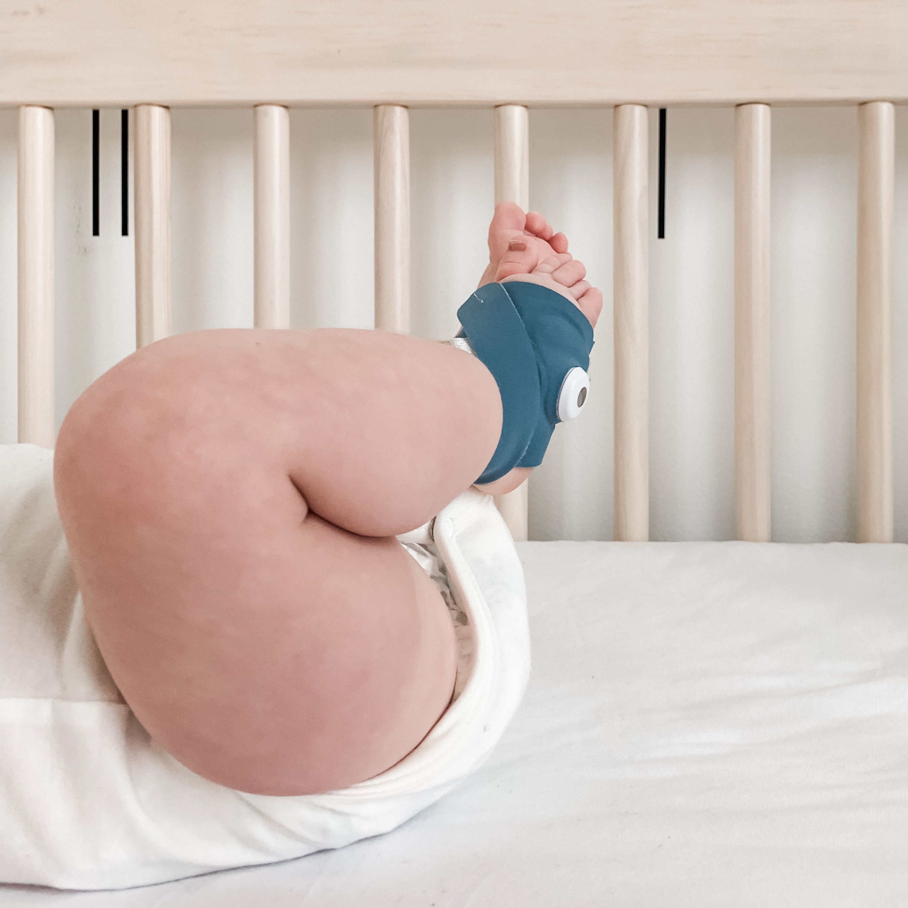 Babyfuß mit Owlet Dream Sock® am Knöchel, neben einem Babybett.