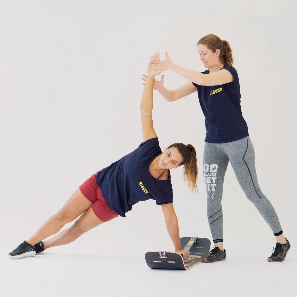 Person macht seitliche Plank-Übung auf GIBOARD SET - CAESAR JIB, Trainer unterstützt.