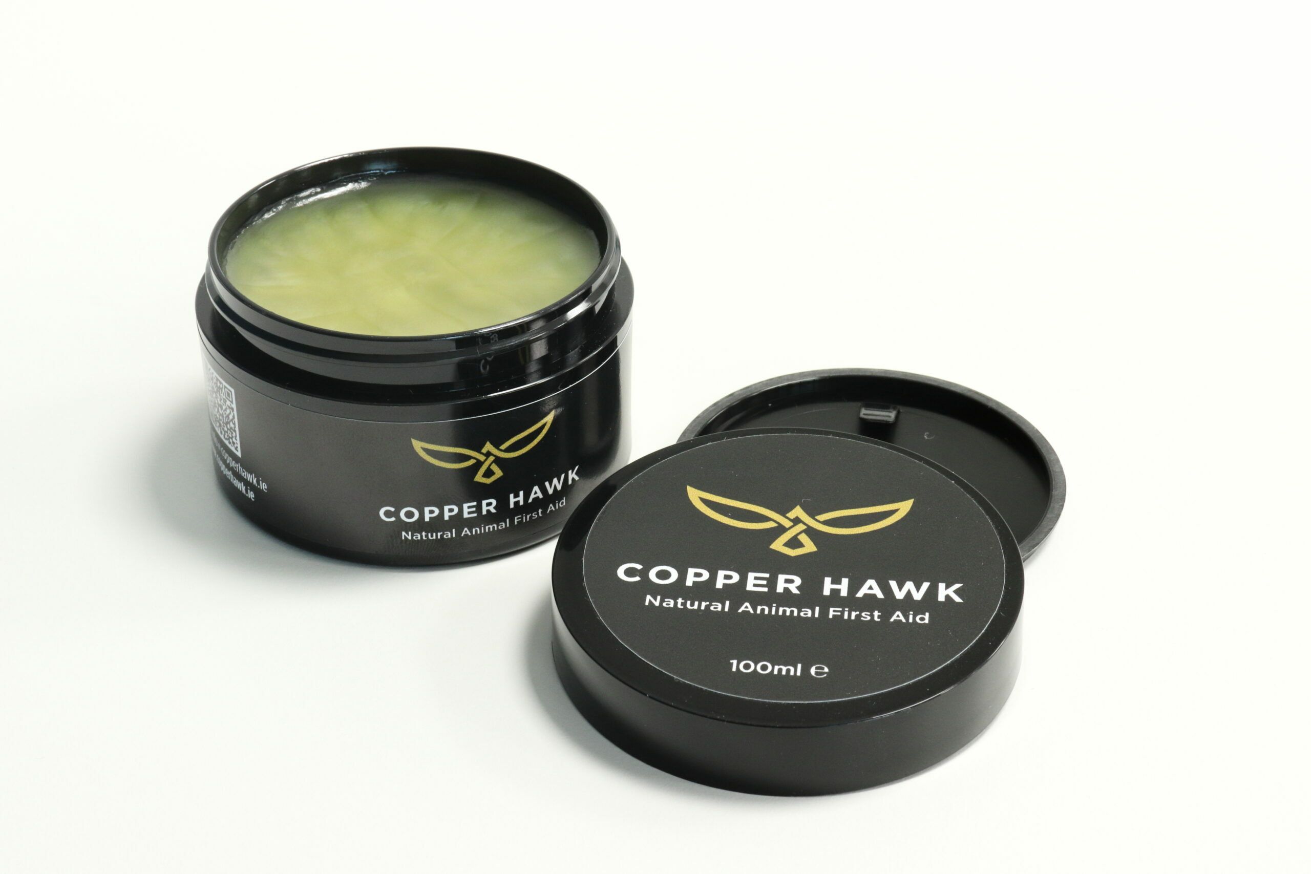 Schwarze Dose mit Deckel. Aufschrift: Copper Hawk, Natural Animal First Aid. Offene Dose mit grünlichem Inhalt. Deckel daneben.