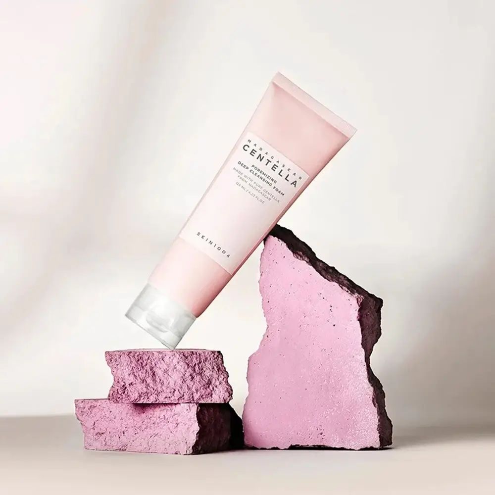 Rosa Tube auf rosa Steinen. Text: MADAGASCAR CENTELLA, Poremizing Deep Cleansing Foam. Marke SKIN1004.
