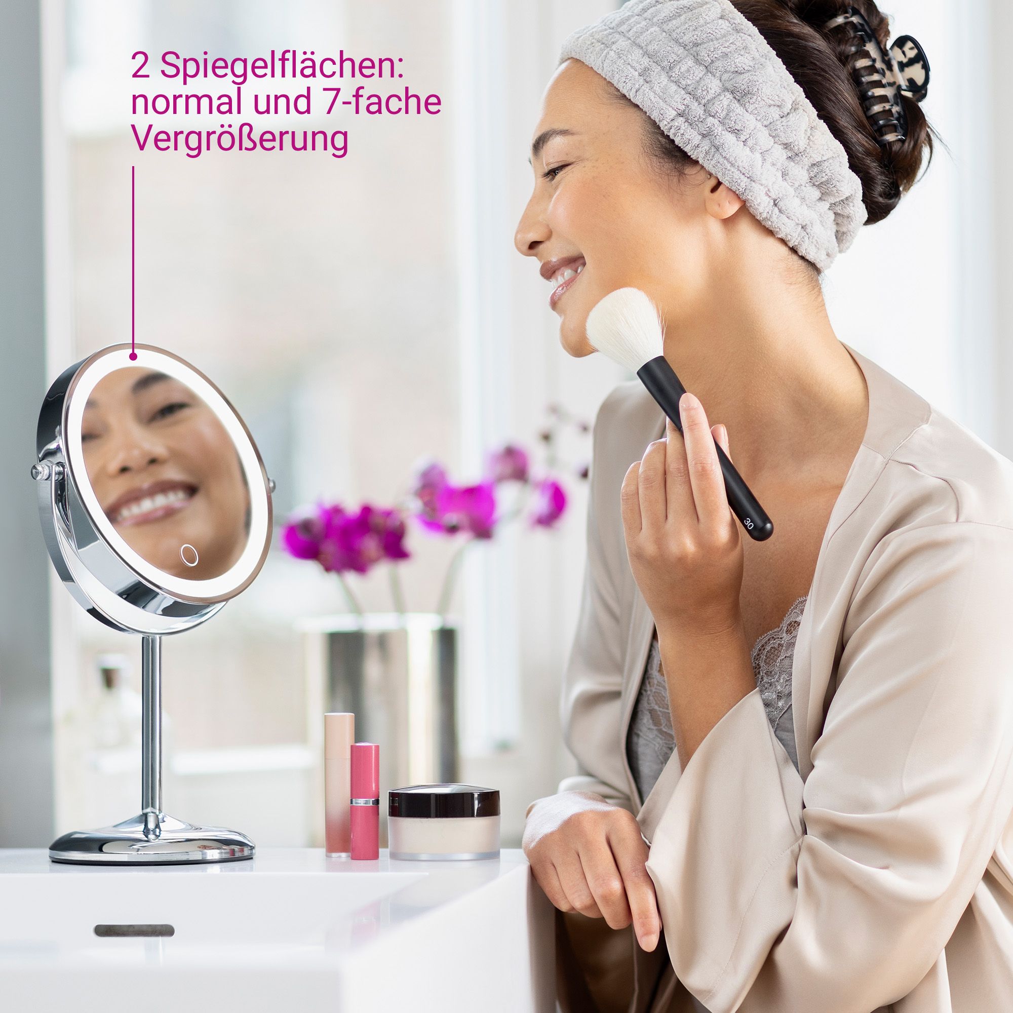Frau trägt Make-up mit Pinsel vor beleuchtetem Kosmetikspiegel (7-fache Vergrößerung).