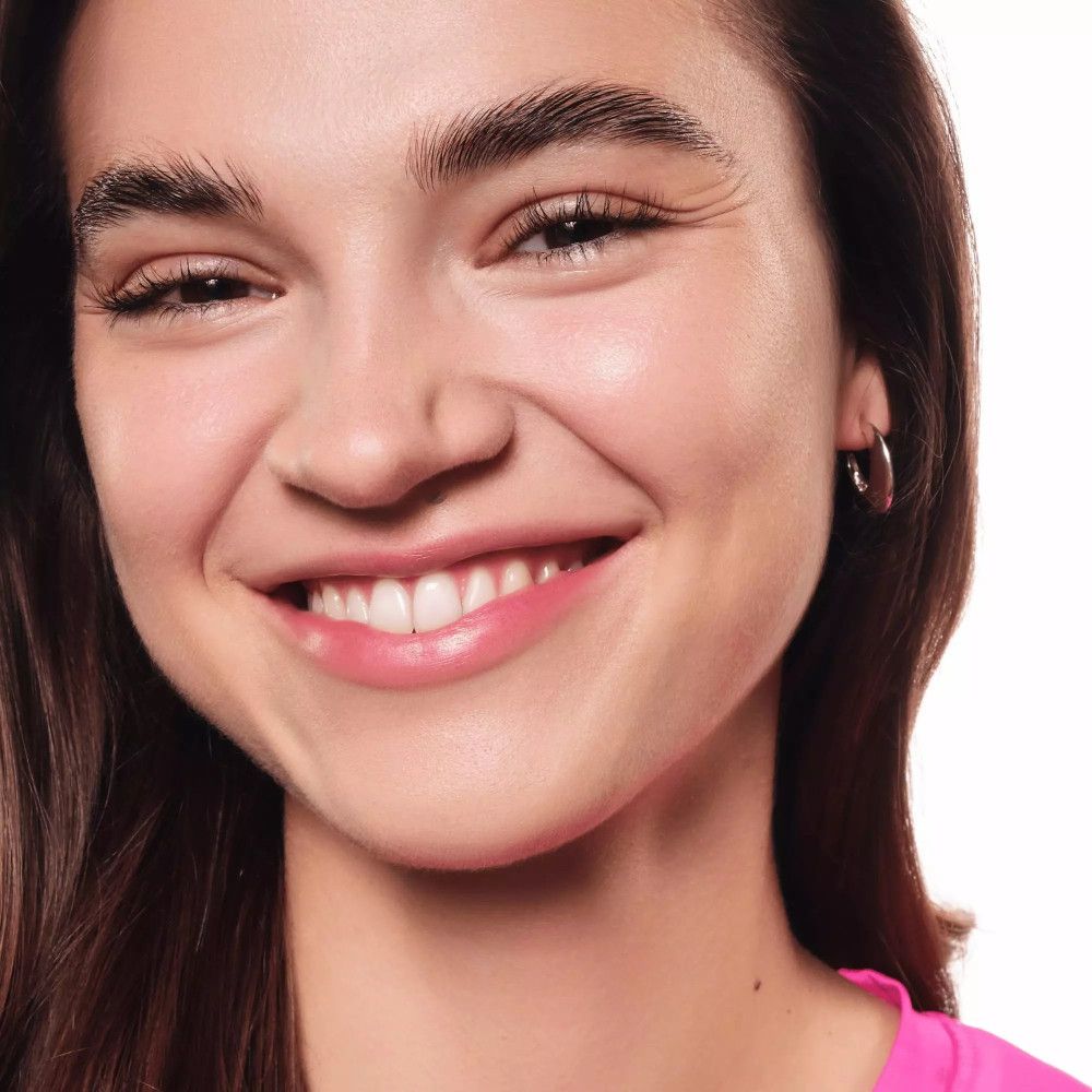 Nahaufnahme einer lächelnden Frau mit braunem Haar und Ohrringen. Sie trägt ein pinkfarbenes Top.