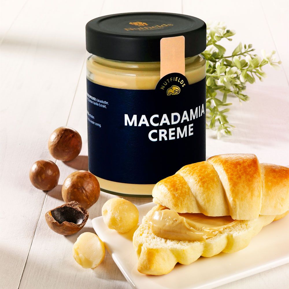 Glas Macadamia Creme mit Nutfields Logo, daneben Macadamianüsse und ein Croissant mit Creme.