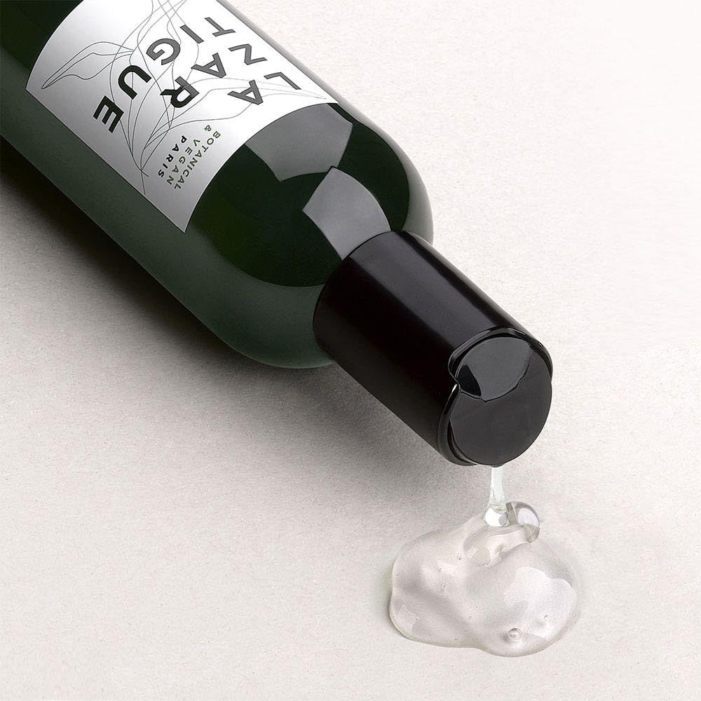 Grüne Flasche mit schwarzem Verschluss, Flüssigkeit tropft heraus. Aufschrift: LA ZAR TIGUE.