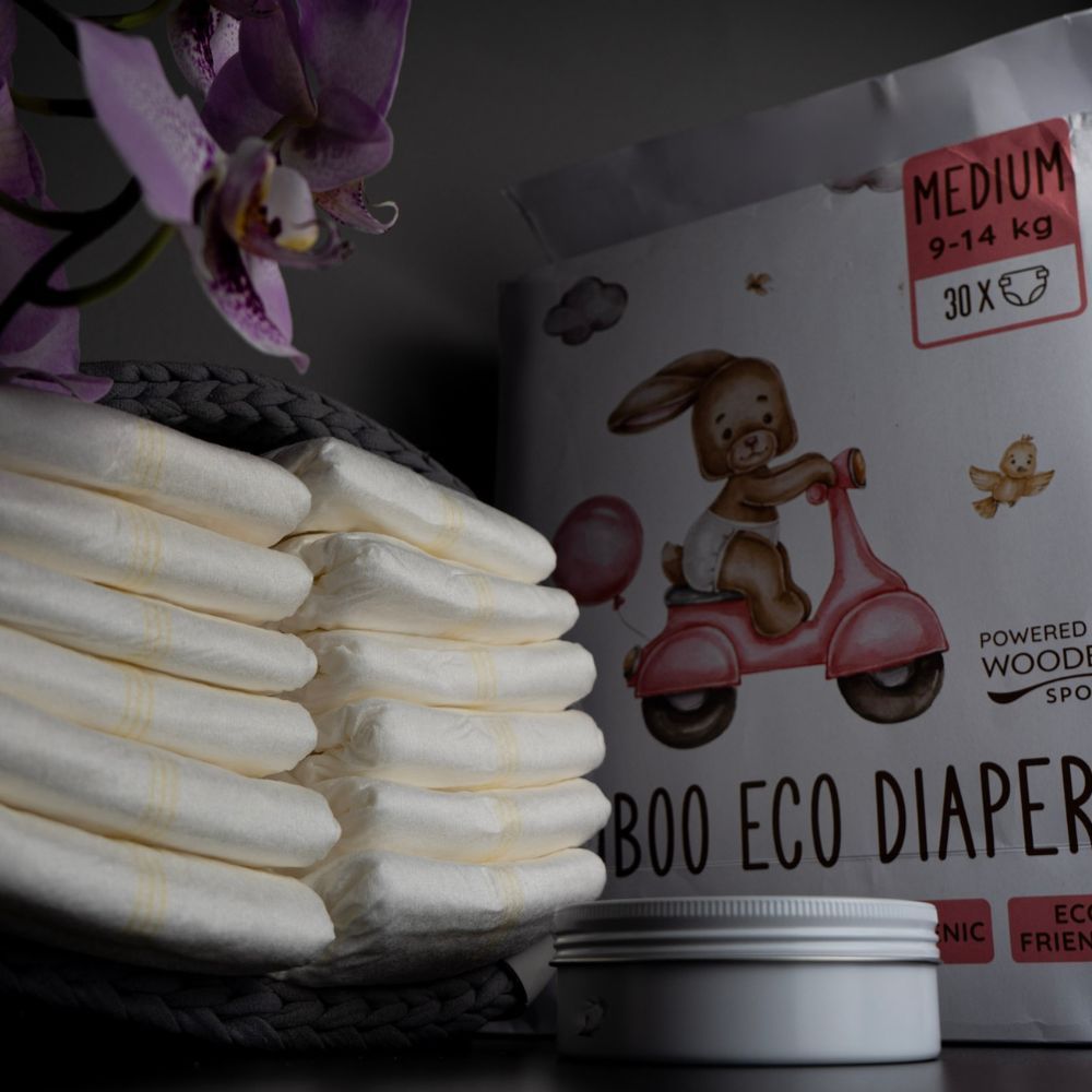 Windelpackung neben gefalteten Windeln in Korb und Cremebehälter. Hintergrund: Orchideenblüten.