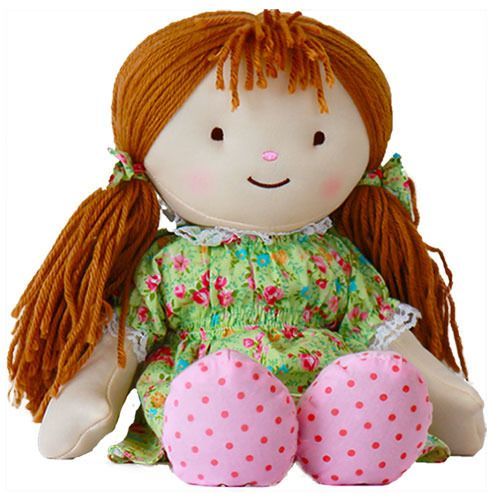Stoffpuppe mit rotem Haar, grünem Kleid mit Blumenmuster und rosa gepunkteten Füßen. Gesicht mit Augen, Nase und Mund.