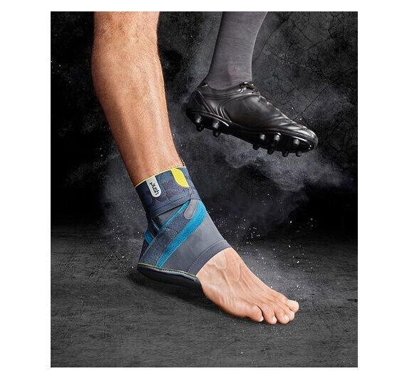 OFA Push Sports Knöchelbandage Kicx am Knöchel eines Fußes. Fußballschuh im Hintergrund. Dunkler Hintergrund.