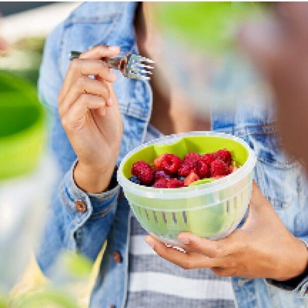 Person hält einen grünen Obstkorb mit Beeren. Die Person isst mit einer Gabel.