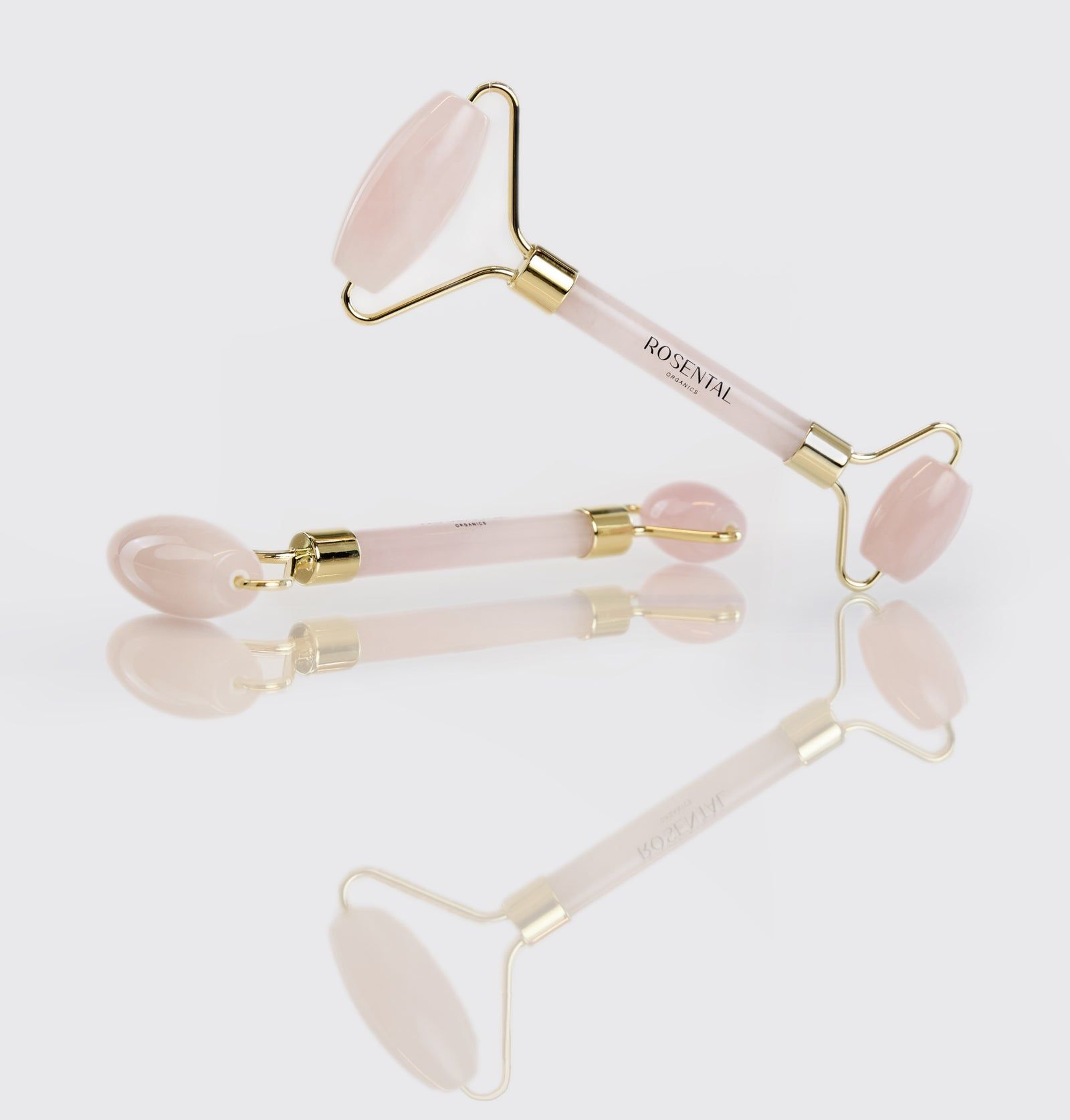 Drei Rose Quartz Roller auf weißem Hintergrund. Goldfarbene Rahmen, rosa Rollen. Produktname sichtbar.