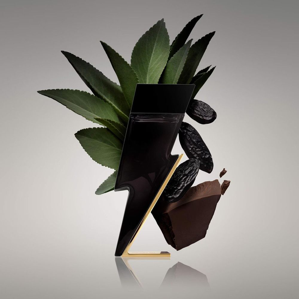 Schwarzer Flakon in Blitzform, goldfarbener Fuß, umgeben von Blättern, Früchten und Schokoladenstück.