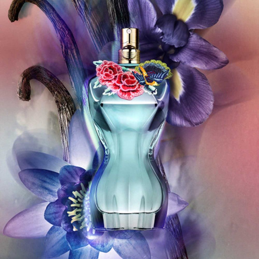 Türkis geformter Flakon mit goldenem Verschluss, verziert mit roten Rosen und einem blauen Schmetterling. Umgeben von Blumen.
