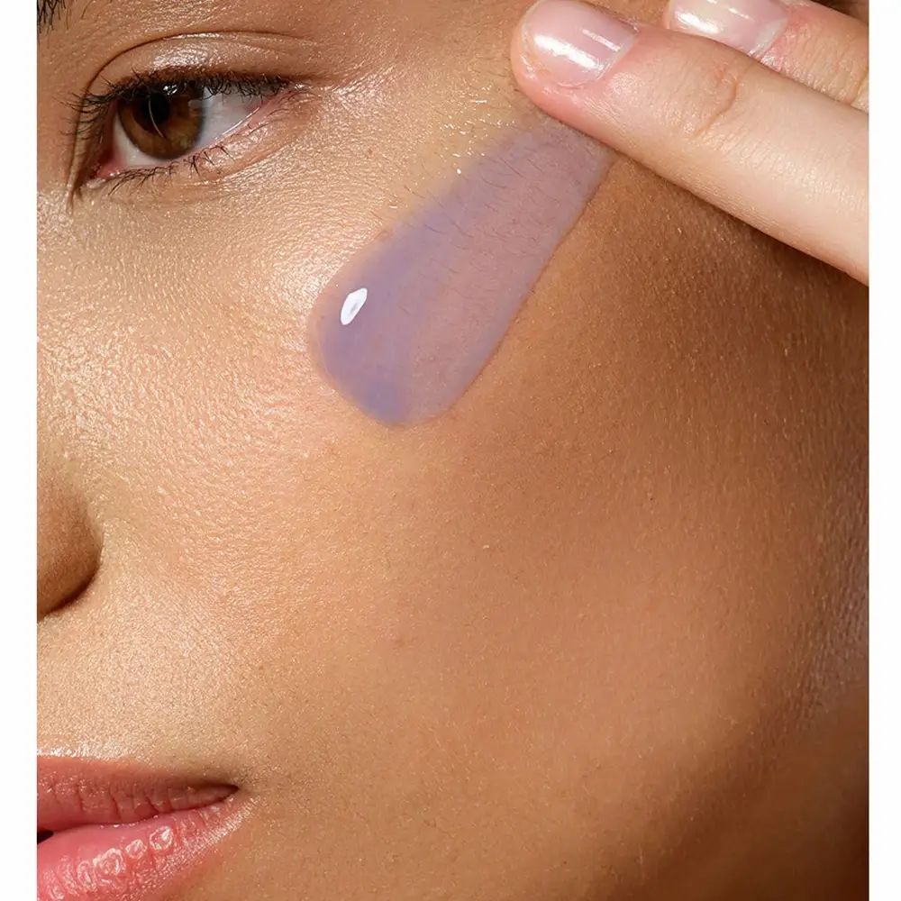 Person trägt Serum auf die Haut auf. Das Serum ist lila und transparent.