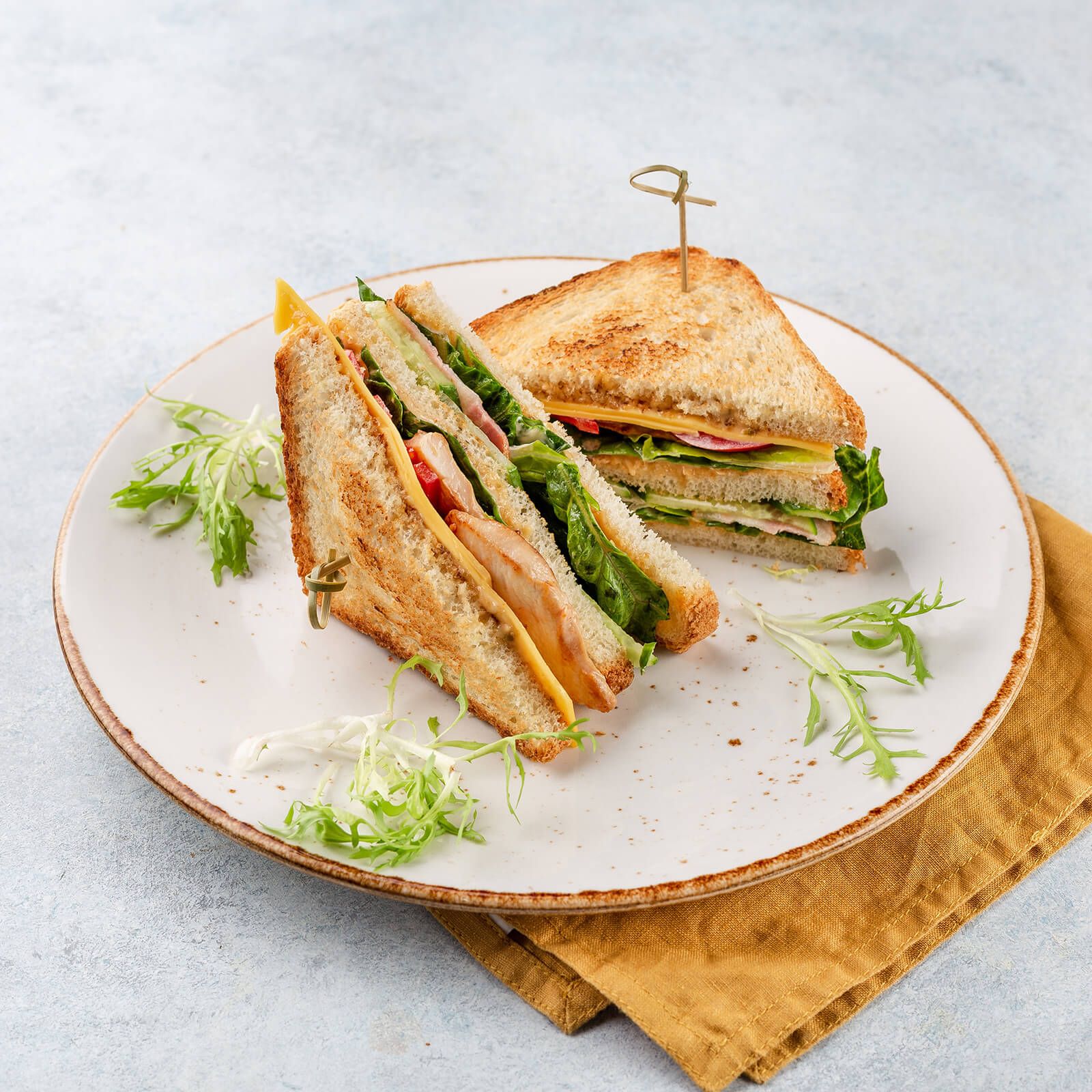 Club-Sandwiches mit Hühnchen, Käse, Salat und Tomaten auf einem Teller.