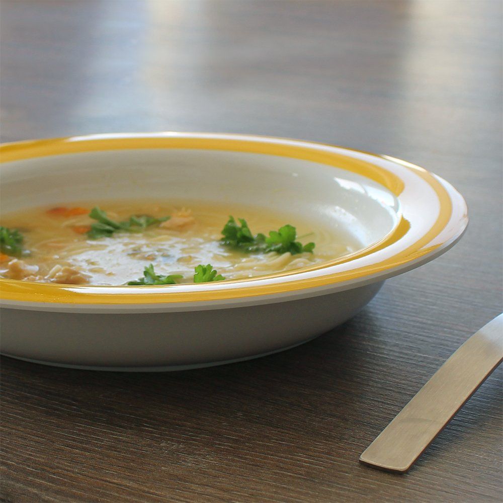 Teller mit gelbem Rand, gefüllt mit Suppe und Petersilie. Auf Holztisch, daneben Löffel.