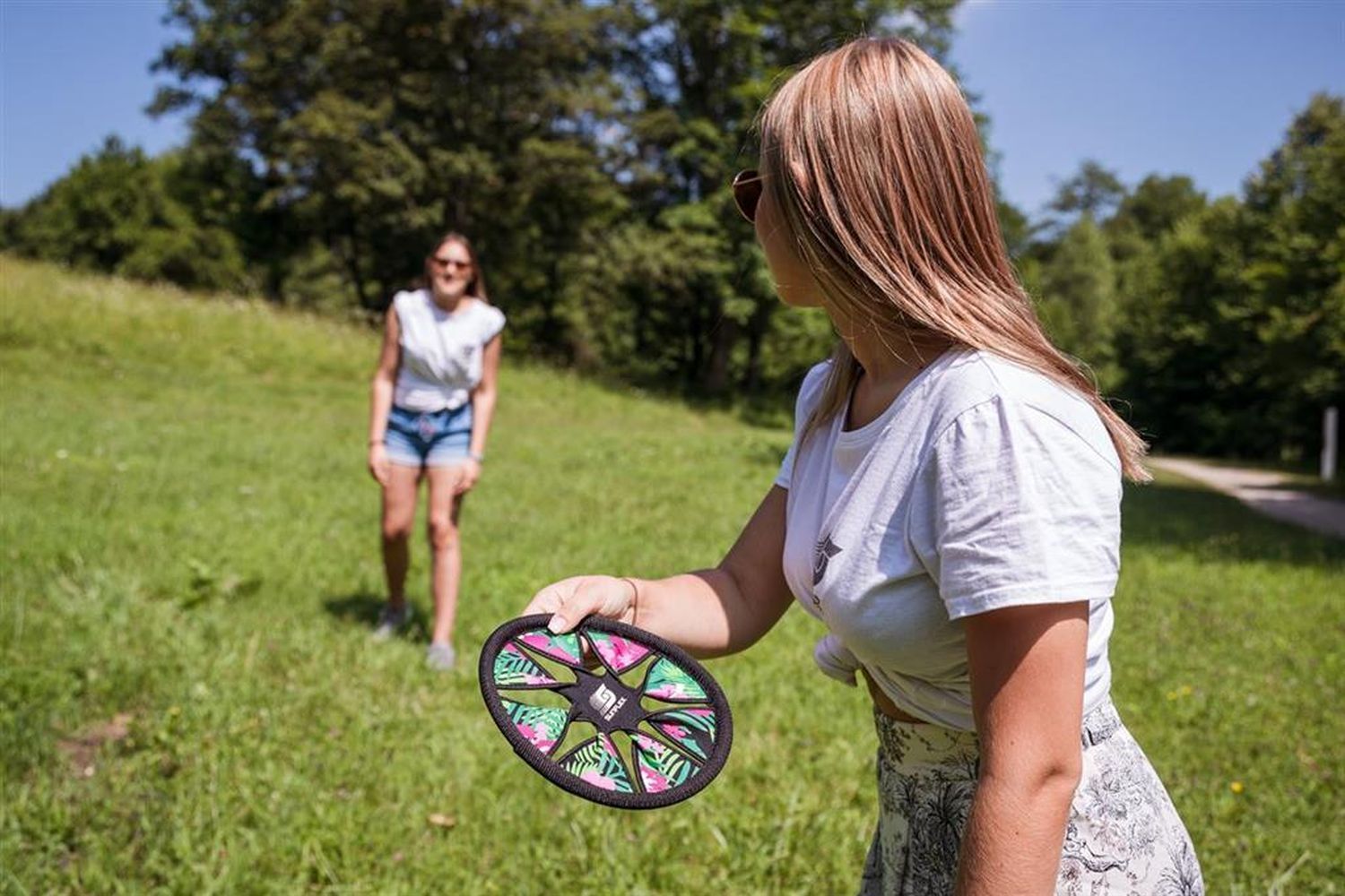 Frau wirft einen Sunflex Flying Disk mit tropischem Blumenmuster. Auf einer Wiese.