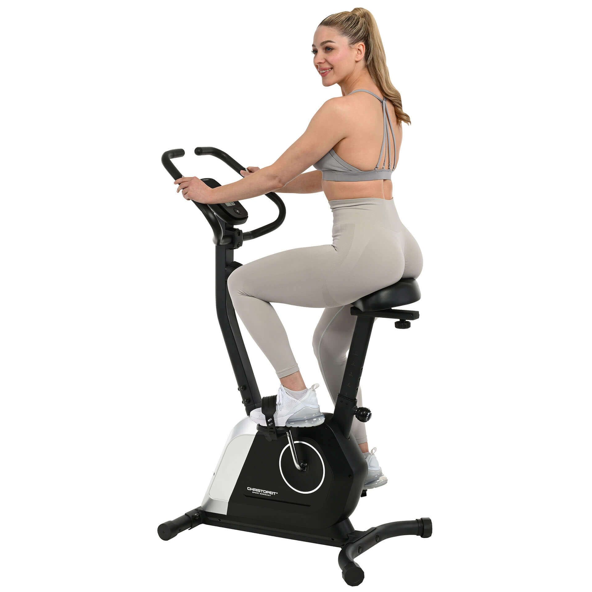 Heimtrainer Activ. Schwarzer Rahmen, silberne Akzente. Frau sitzt auf dem Sattel und trainiert. Digitalanzeige.