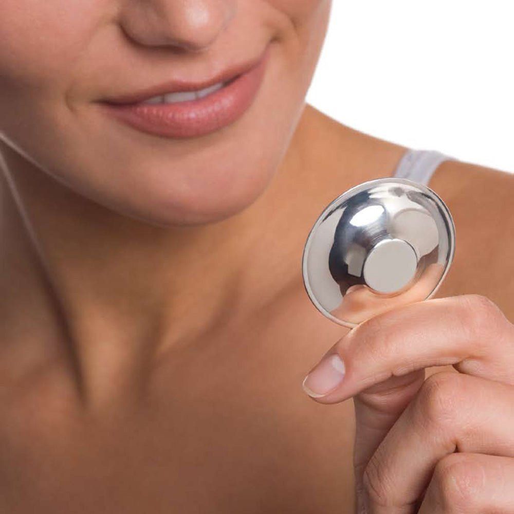 Silberfarbener Brustwarzenschutz, gehalten von einer Person. Runde Form mit erhabenem Mittelteil.