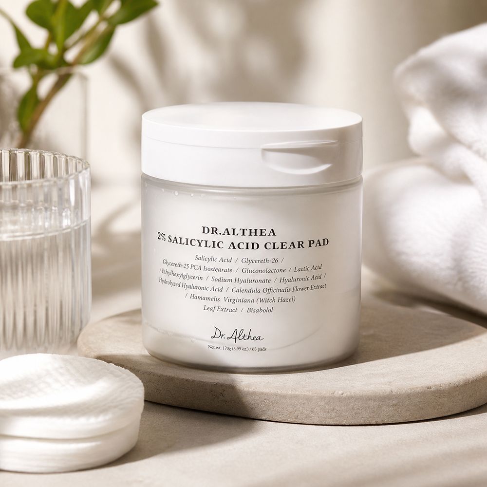 Dr. Althea 2% Salicylsäure Clear Pad auf einem Steinpodest, neben Wattepads und einem Glas.