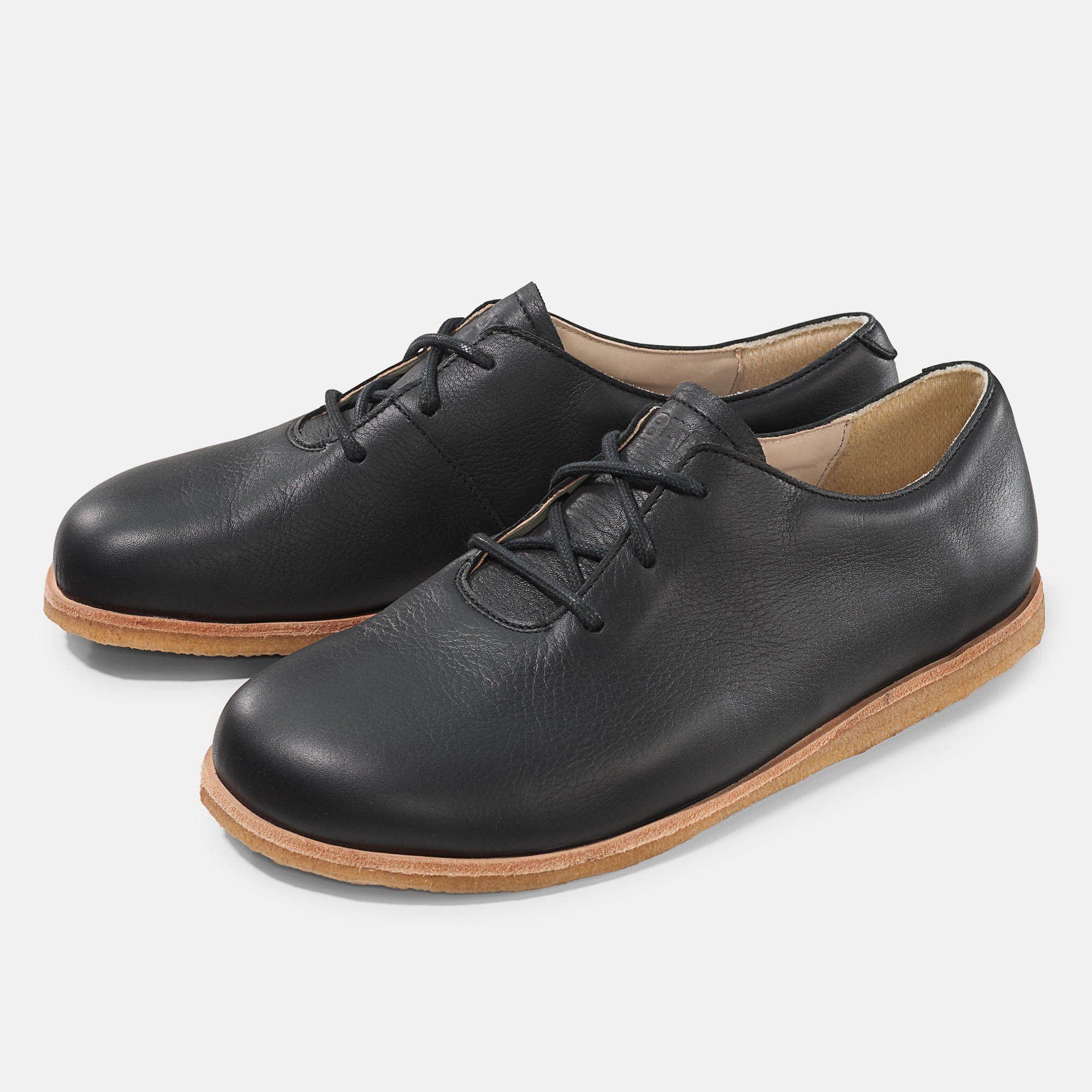 Schwarze Lederschnürschuhe mit heller Sohle. Zwei Schuhe nebeneinander, Ansicht von oben. Schnürsenkel sichtbar.