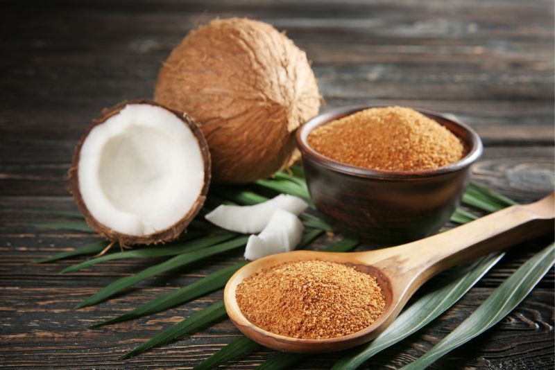 Kokosnuss, Kokosnuss-Hälften, Kokosblütenzucker in Schale und Löffel, auf Holzuntergrund.