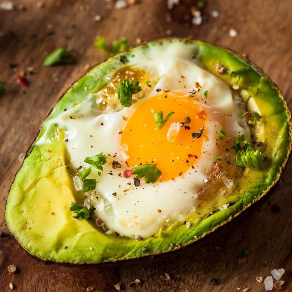 Halbe Avocado mit Spiegelei. Eigelb in der Mitte, Kräuter und Pfeffer. Auf Holzuntergrund.