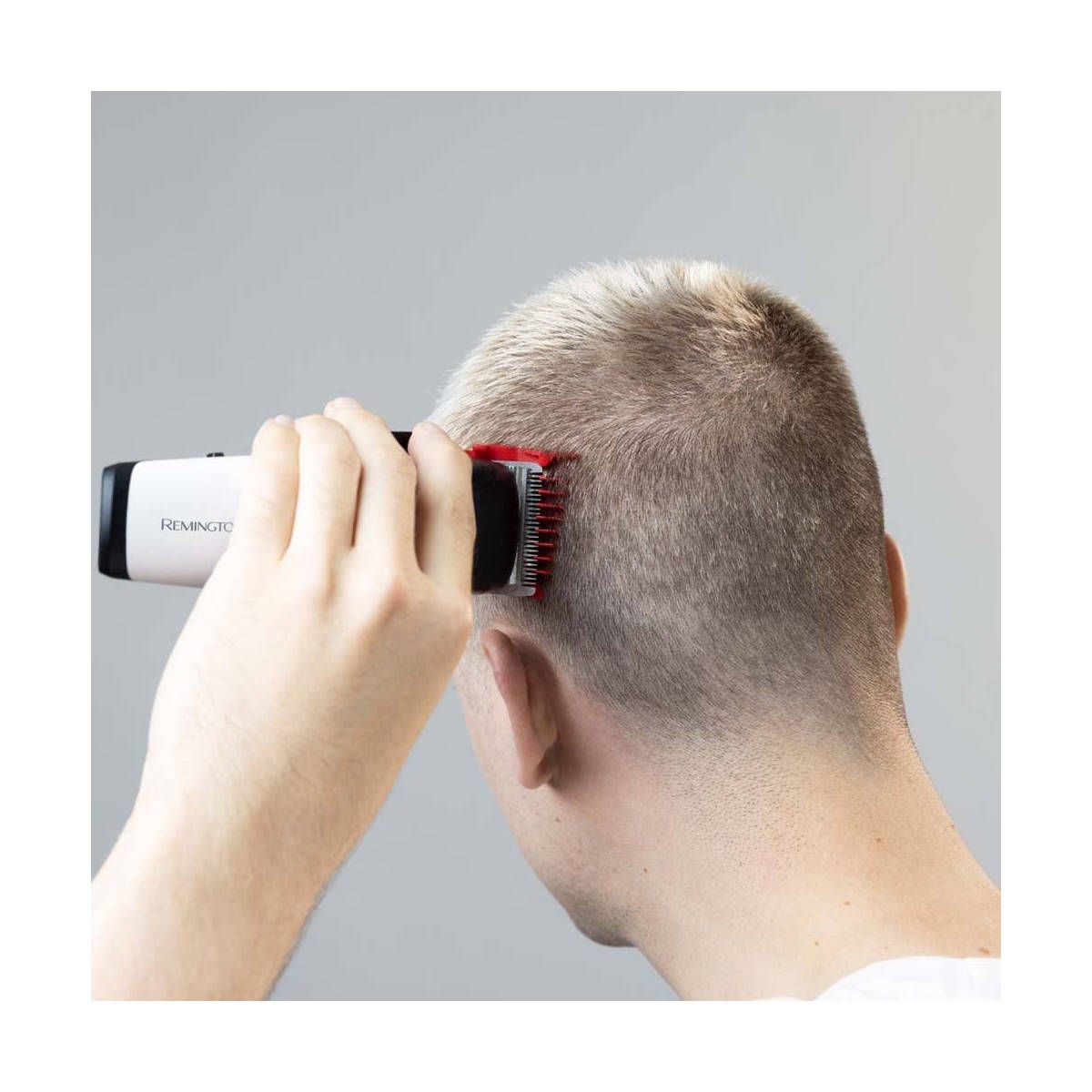 Mann schneidet sich die Haare mit einem Haarschneider. Weißes Gehäuse, roter Aufsatz. Grauer Hintergrund.