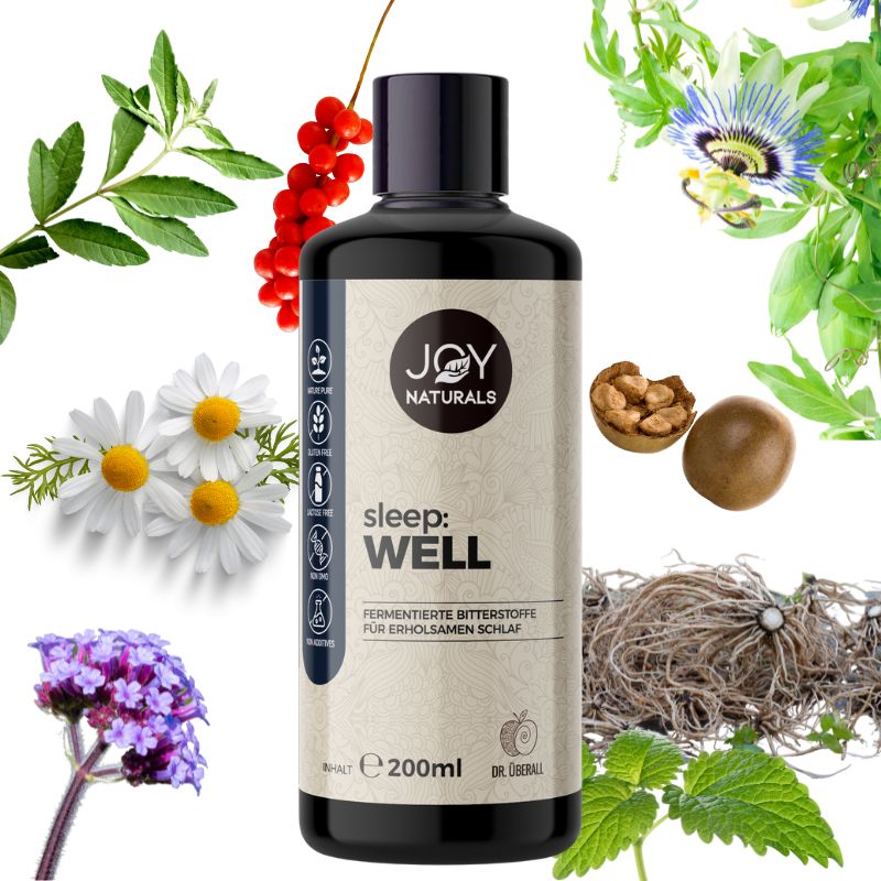 JOY NATURALS Schlaf-Komplex Flasche, umgeben von Kräutern und Blüten. Schwarz, zylindrisch. Etikett.