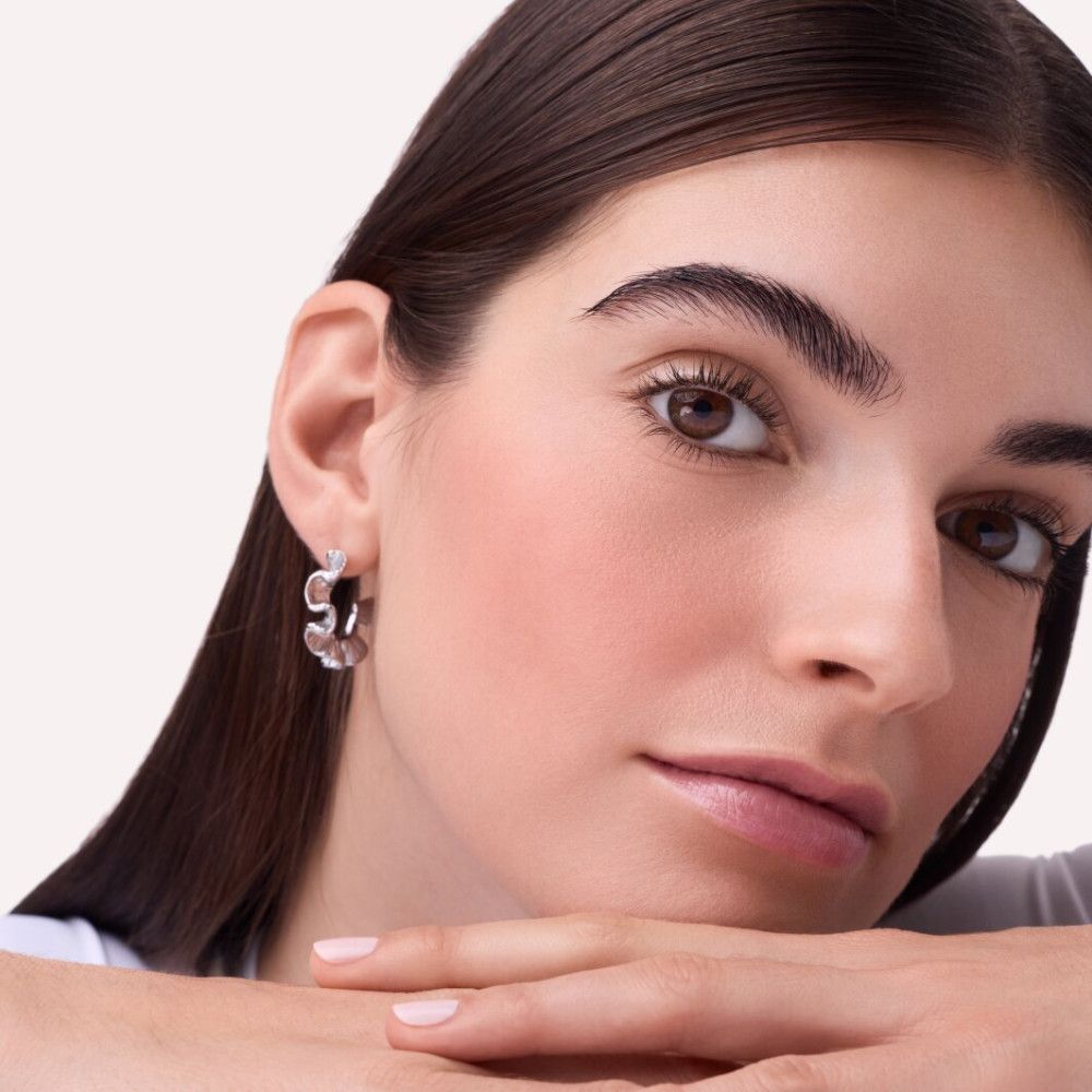 Porträt einer Frau mit Rouge auf den Wangen. Sie stützt das Kinn auf die Hände.