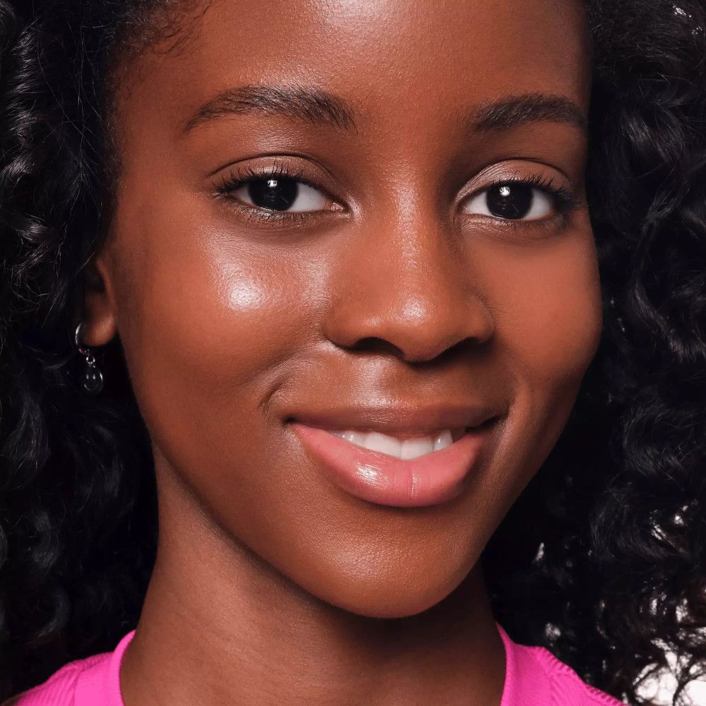 Porträt einer Frau mit glatter Haut. Sie trägt rosa Oberteil und hat Concealer aufgetragen.