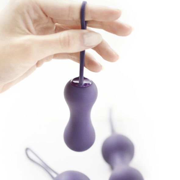 Hand hält eine violette progressive Geisha-Kugel mit Schnur. Andere Kugeln unscharf im Hintergrund.