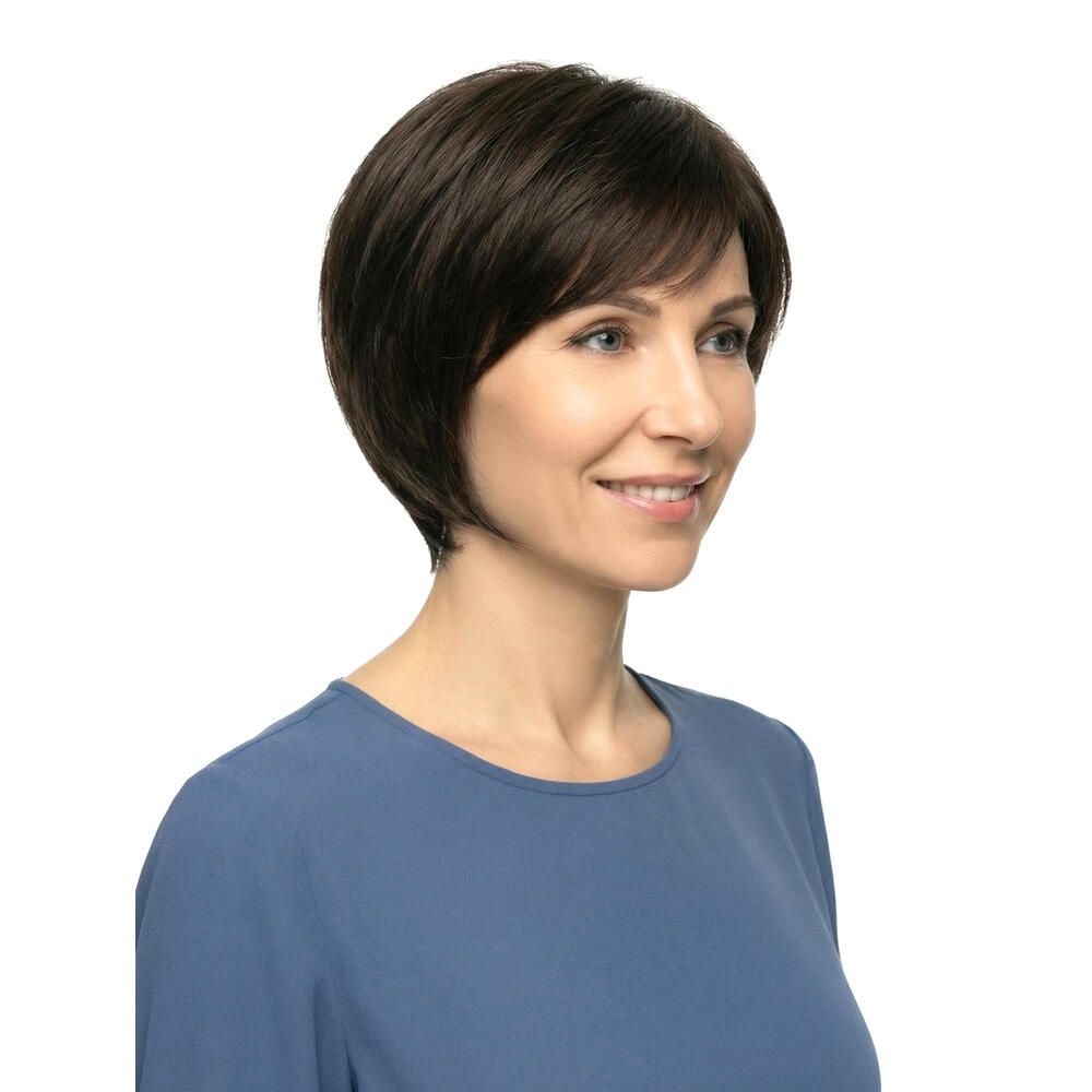 Kurzhaarperücke, braun, mit Pony, von einer Frau getragen. Die Frau lächelt und trägt ein blaues Oberteil.