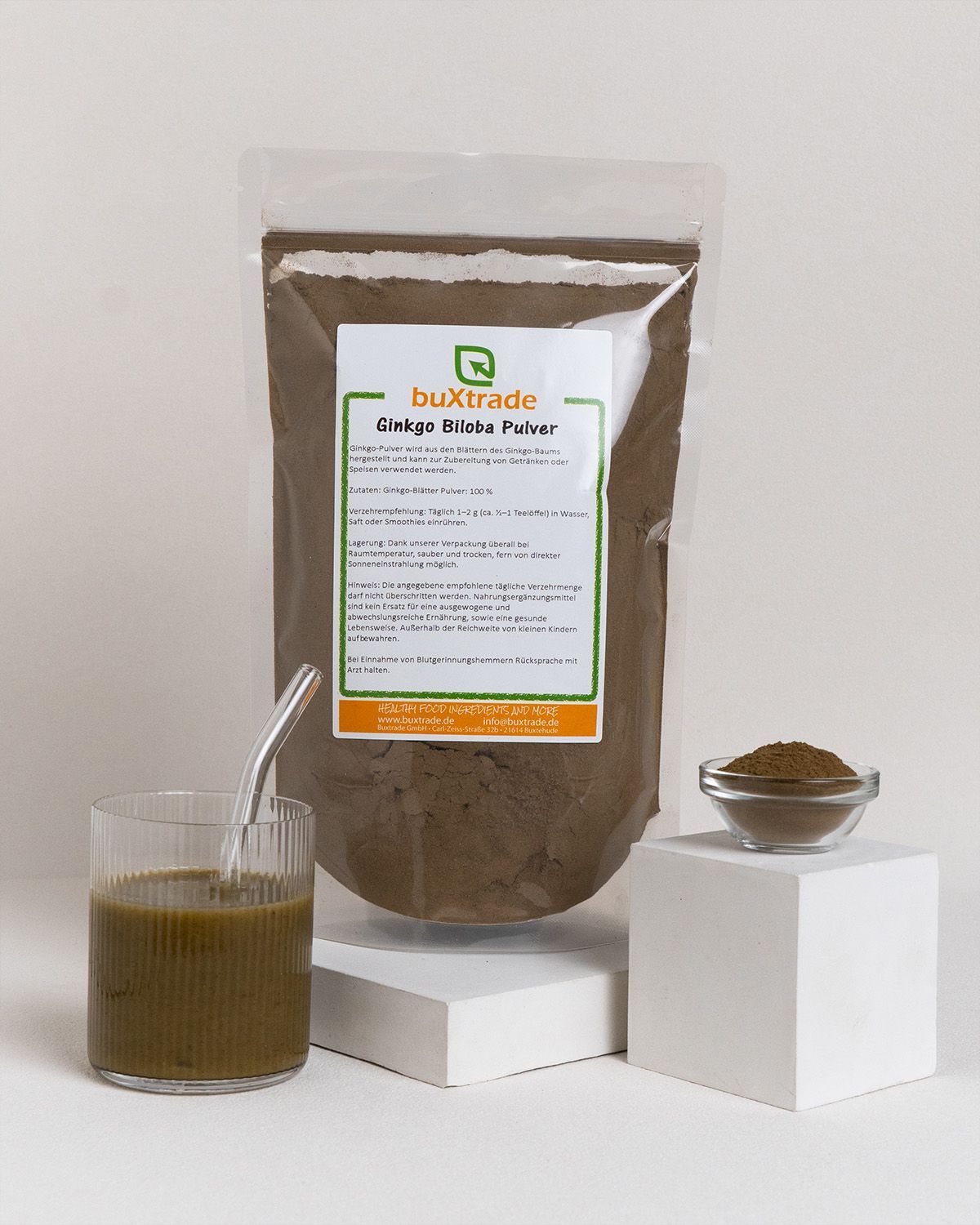 Glas mit Flüssigkeit, Schüssel mit Pulver und Beutel. Beutel mit Aufkleber: buXtrade Ginkgo Biloba Pulver.